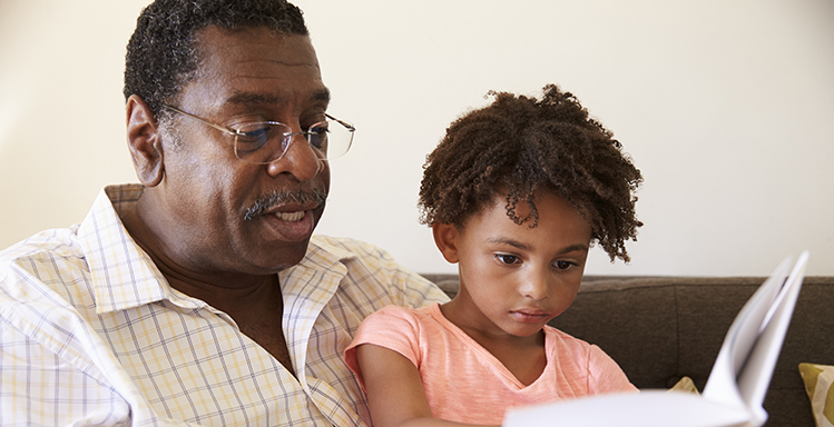 Grandfather And Granddaughter Reading Book At Home Together