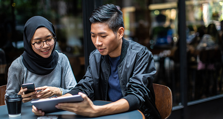 Two people having fun in the cafe outdoors, eating cake and drinking coffee, using technology